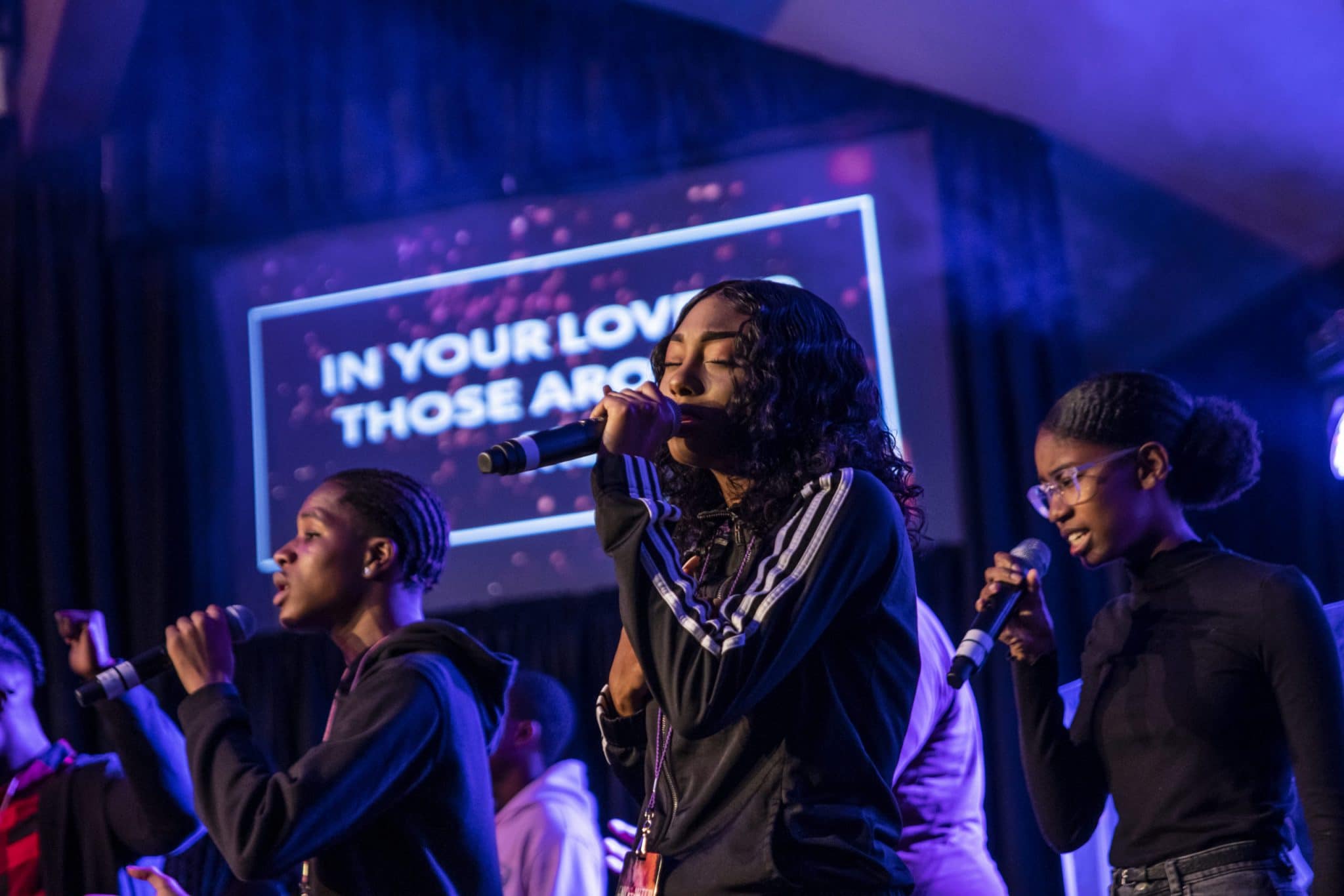 Two girls and a boy wearing black shirts singingsinging on stage