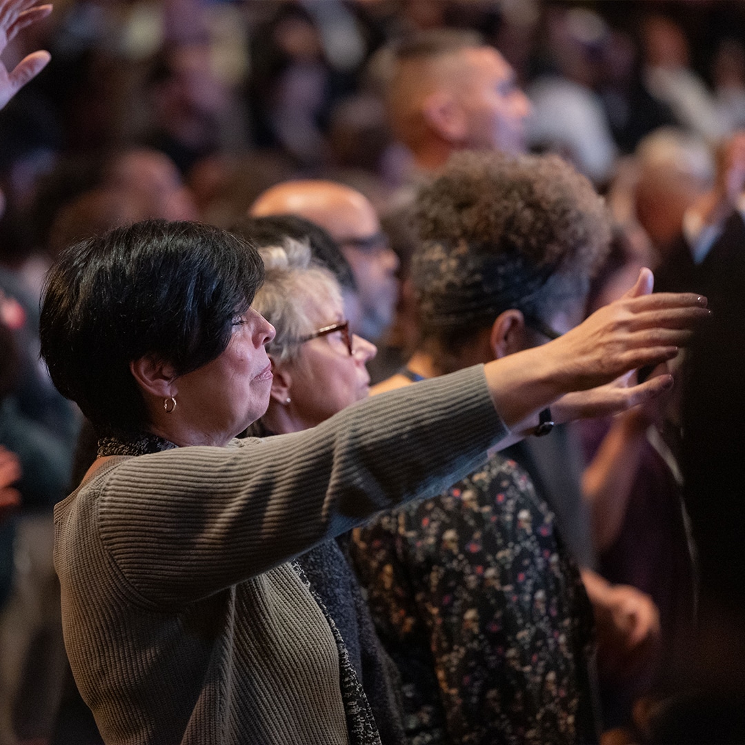 woman worshipping with hand lifted in front of other congregants