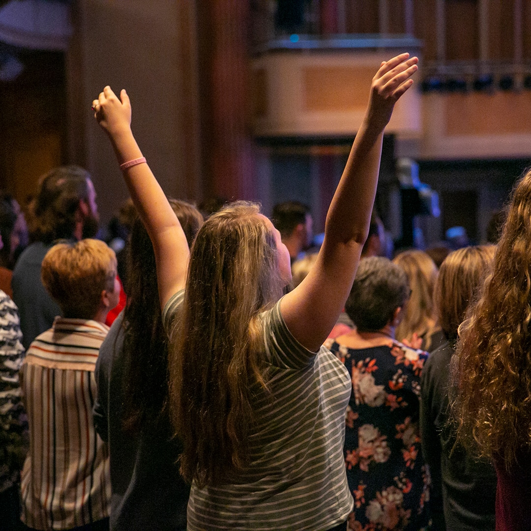 woman in sanctuary with both hands lifted to God
