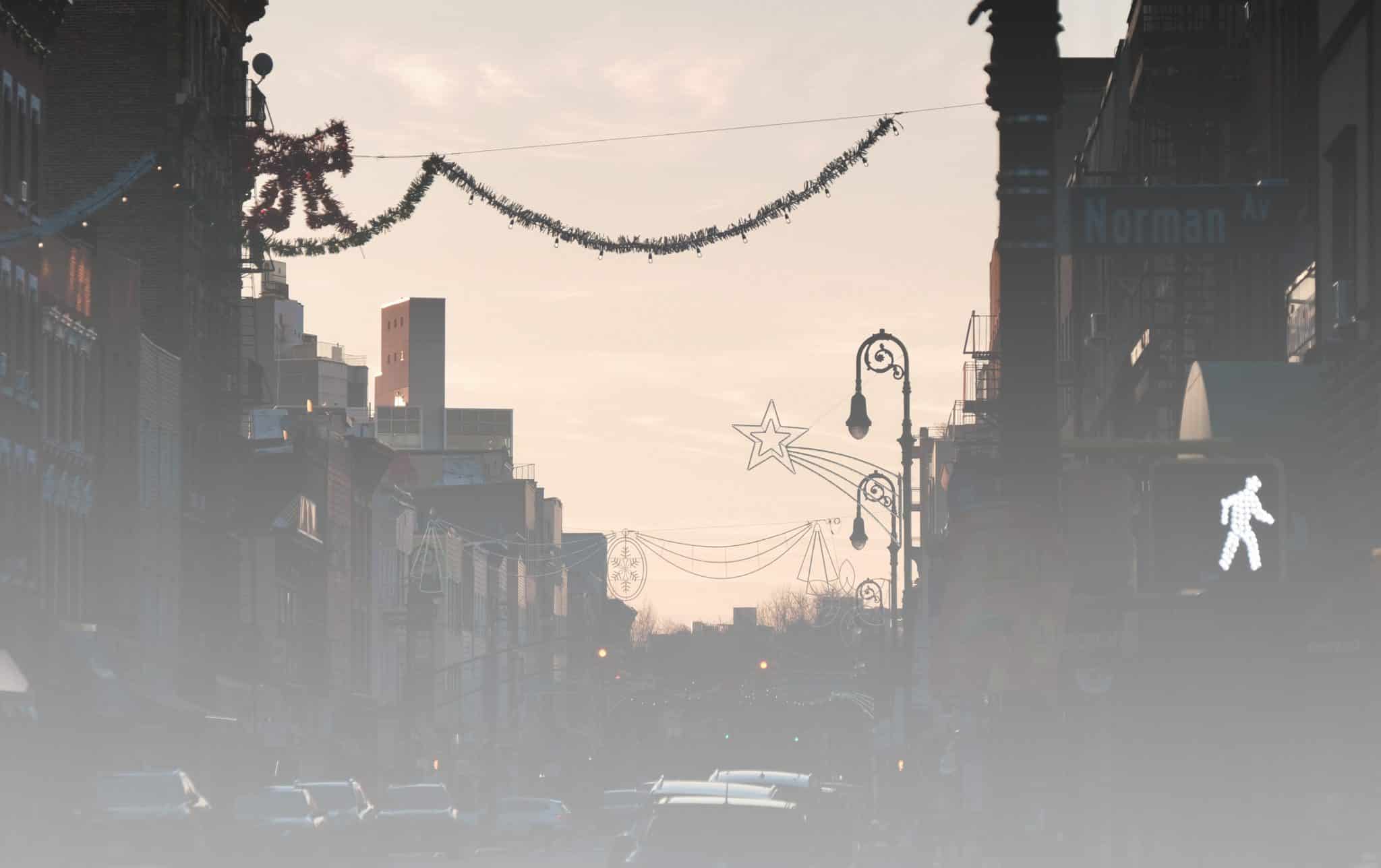 Brooklyn street with Christmas garlands and bright sky shining into dark below