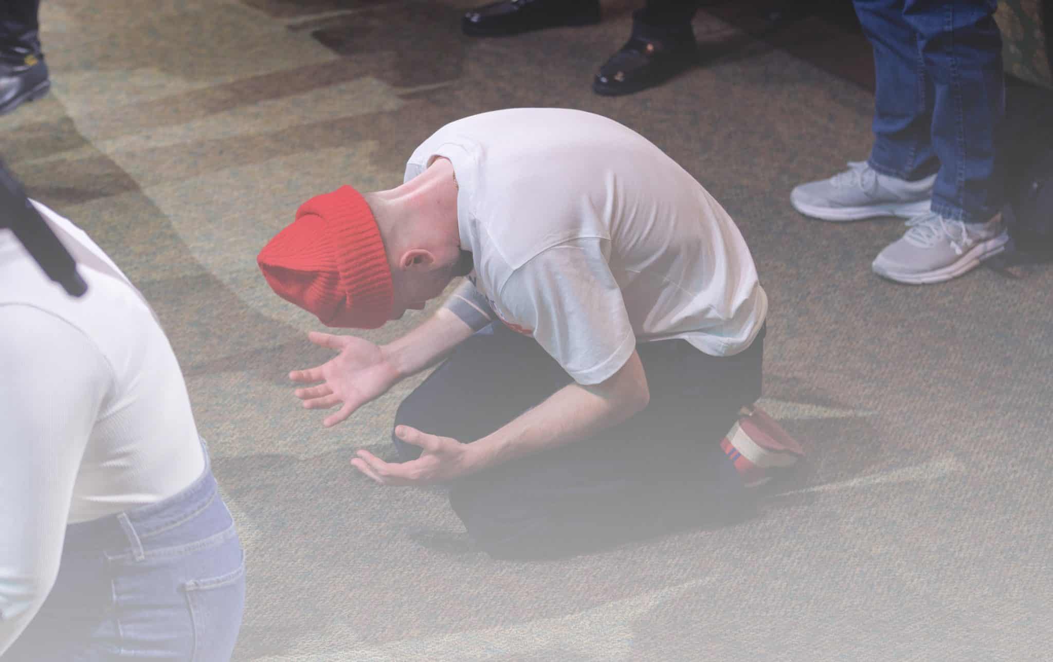 Man with red hat kneeling and bowing before God in prayer